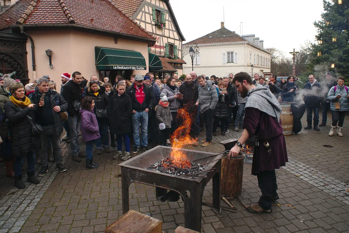 Blacksmith working a fire while a crowd watches at the Ribeauvillé Christmas market